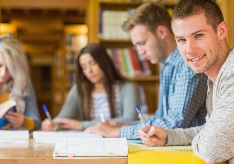 Smiling male student with friends at library